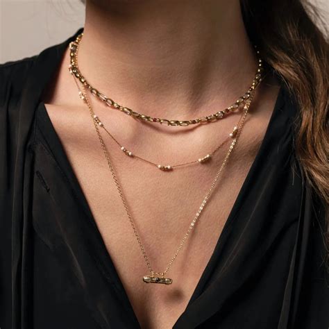 Exemple de superposition de trois colliers de longueurs différentes, en or jaune, avec des pendentifs variés.