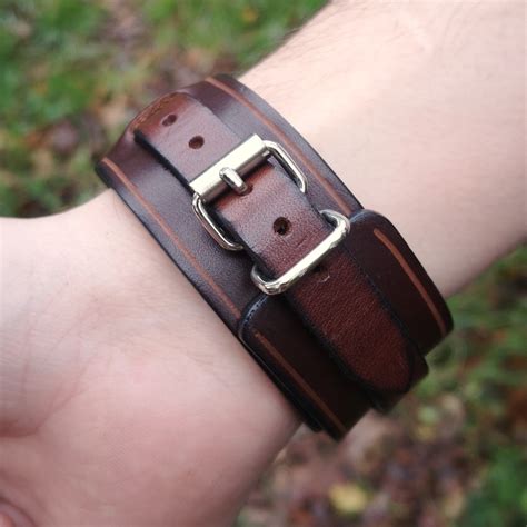 Gros plan sur un bracelet force en cuir marron orné d'un concho gravé de motifs abstraits.