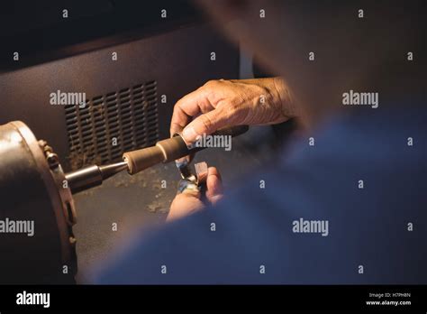 Photographie rapprochée des mains d'une artisane travaillant avec précision sur un bijou, mettant en valeur le savoir-faire.