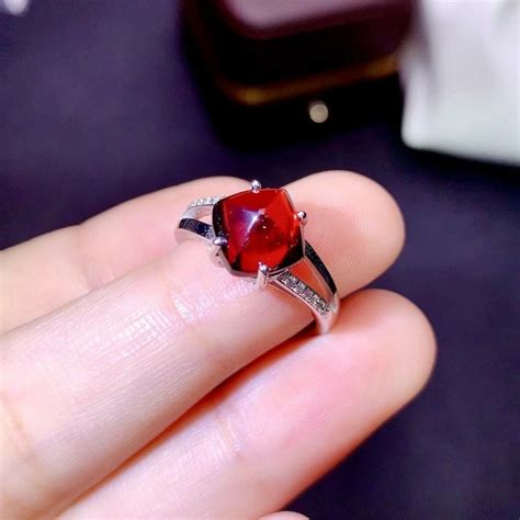 Une bague en grenat rouge sur une monture en argent avec un fond texturé rappelant la terre.