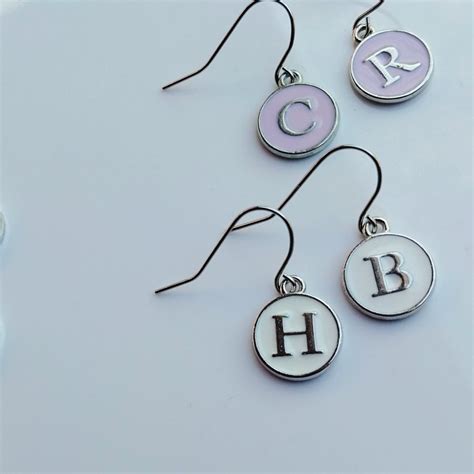 Exemples de boucles d'oreilles personnalisées avec initiales, symboles et motifs colorés.
