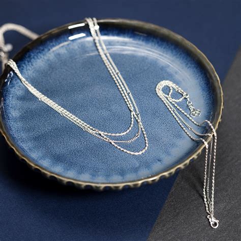 Gros plan sur une parure en Argent 925, montrant un bracelet et un collier avec un motif de rectangles entrelacés, soulignant le design géométrique et moderne.