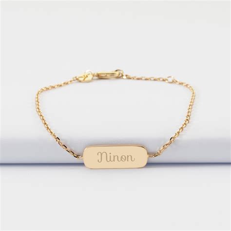 Une main d'enfant tenant délicatement un bracelet en or fin avec une petite médaille gravée.