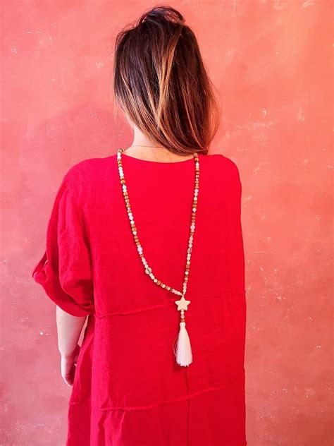 Sautoir rouge avec pompon et perles rouges et argentées, porté sur une tenue décontractée.