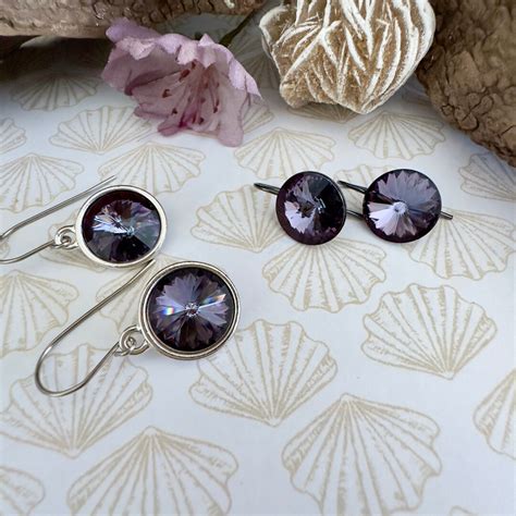 Divers styles de boucles d'oreilles violettes Swarovski, incluant des puces, des pendants et des créoles.