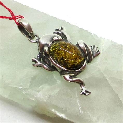 Gros plan sur un pendentif grenouille en argent, mettant en évidence le détail des pattes enserrant une boule d'ambre aux inclusions naturelles.