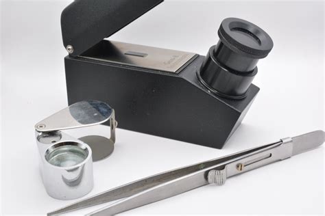 Photographie d'un gemmologue utilisant une loupe et un réfractomètre sur des pierres.