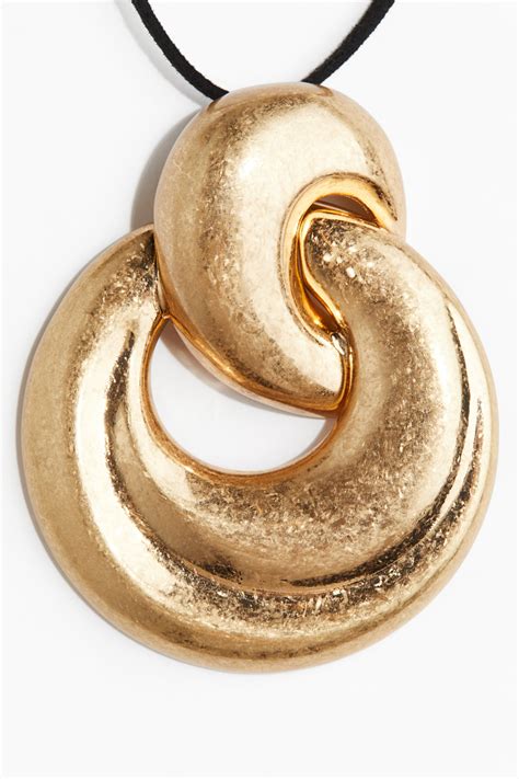 Gros plan sur un collier Swarovski doré avec un pendentif élégant, symbolisant le glamour et la sophistication.