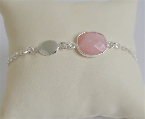 Une main tenant un galet de quartz rose, avec un bracelet fin en argent autour du poignet.