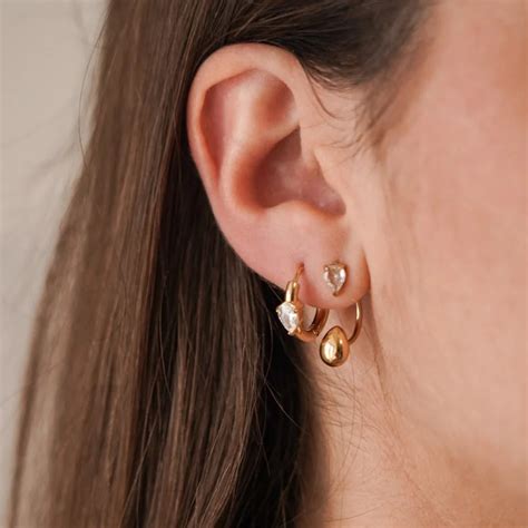 Photographie de plusieurs boucles d'oreilles portées sur différentes perforations d'une oreille, illustrant le 