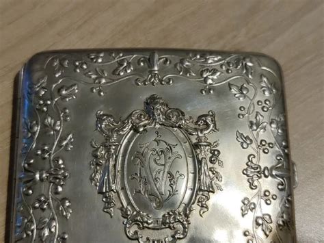 Photographie macro d'un étui à cigarettes en argent massif des années 1930, mettant en évidence les détails de gravure et la qualité du métal.