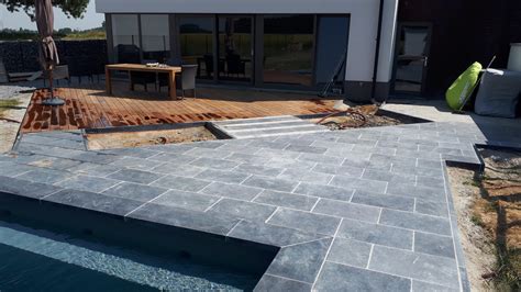 Vue d'une terrasse en pierre bleue avec une piscine environnante.