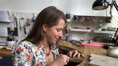 Photo de la créatrice, Maxine, souriante dans son atelier, entourée de bijoux et de matériaux.