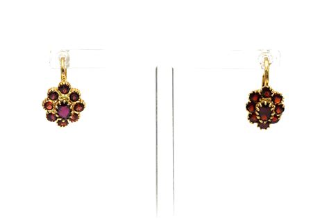 Gros plan sur des boucles d'oreilles en or jaune serties d'une topaze rouge et de petits diamants.