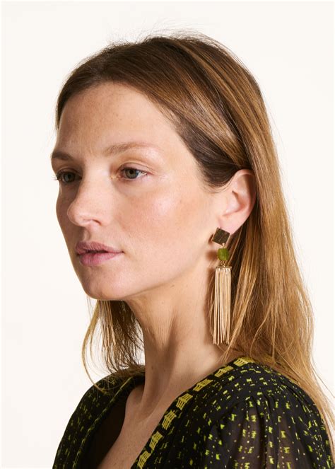 Modèle portant des boucles d'oreilles pendantes dorées qui attrapent la lumière.