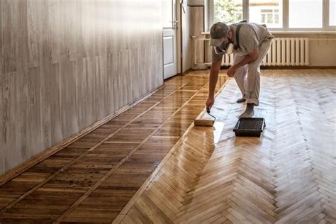 Photo d'un artisan appliquant du vitrificateur sur un parquet fraîchement poncé