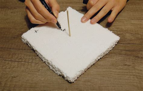 Enfant perforant une feuille de papier avec un cure-dent sur une plaque de polystyrène
